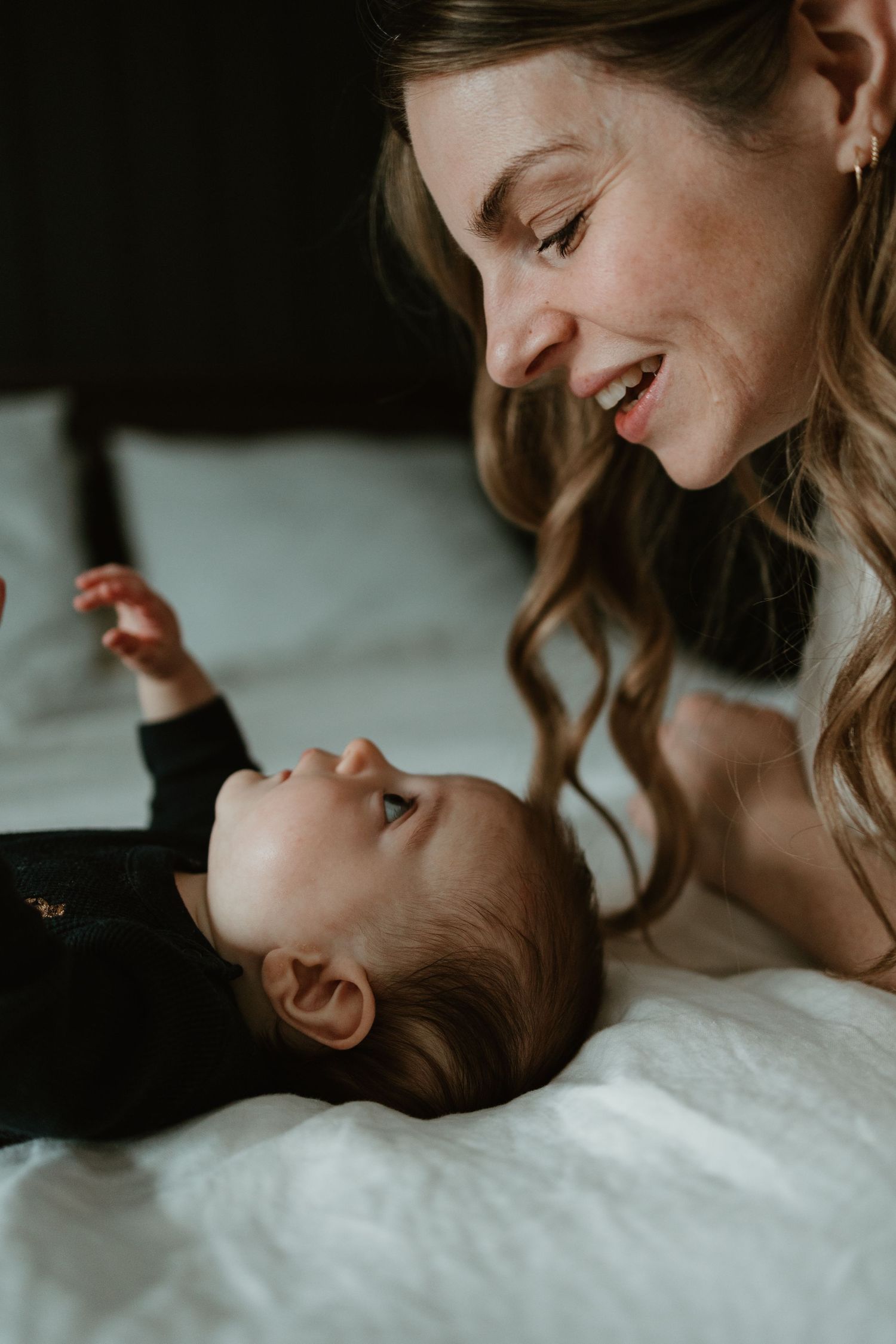 Tender moment between parent and baby lying on white bedding.