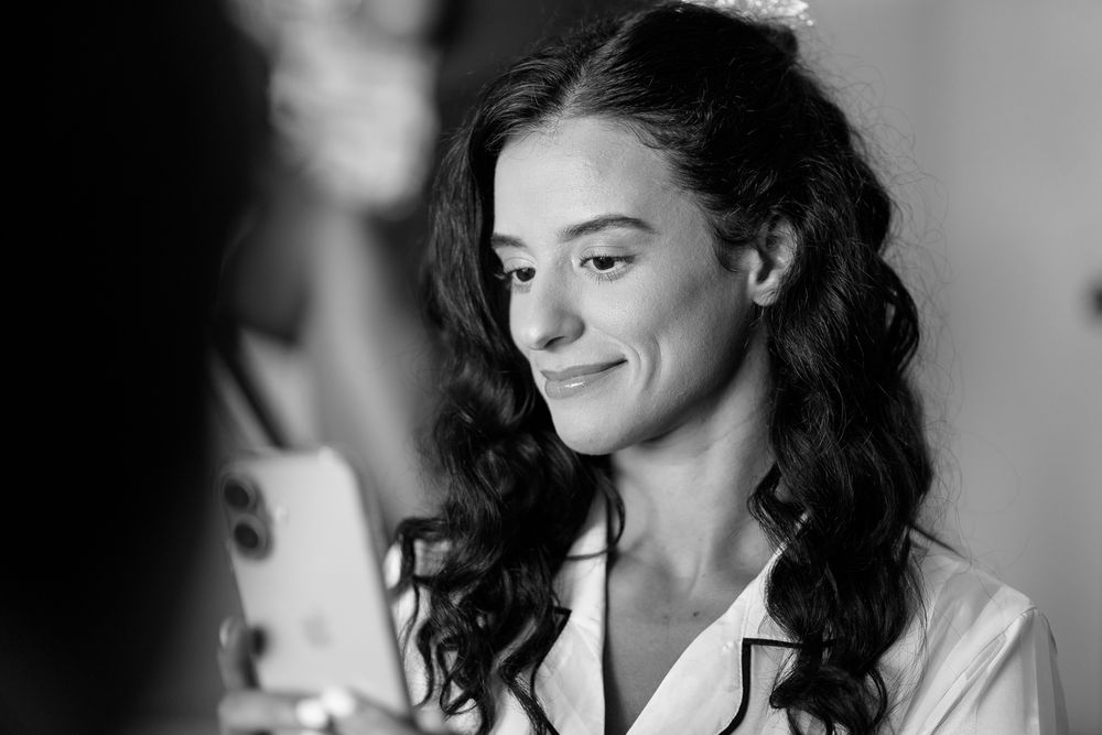 Black and white photo of person with long dark curly hair smiling while wearing a white top.