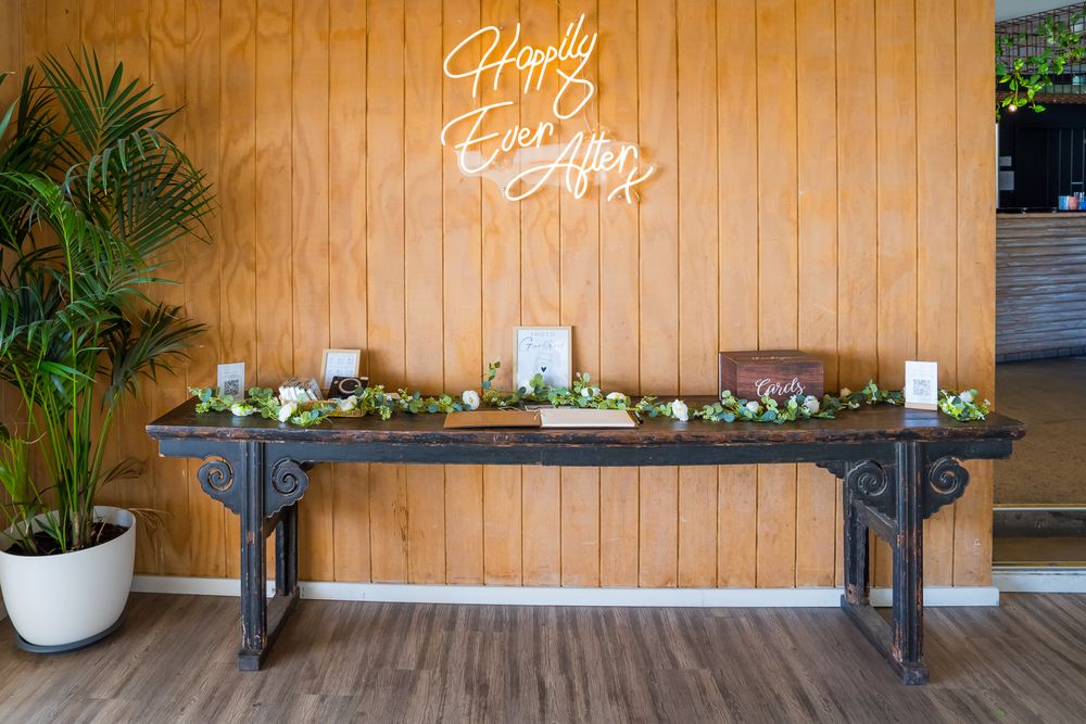 Farmhouse-style buffet table with green garland decor and white candles beneath a glowing 'Happy Easter' neon sign.