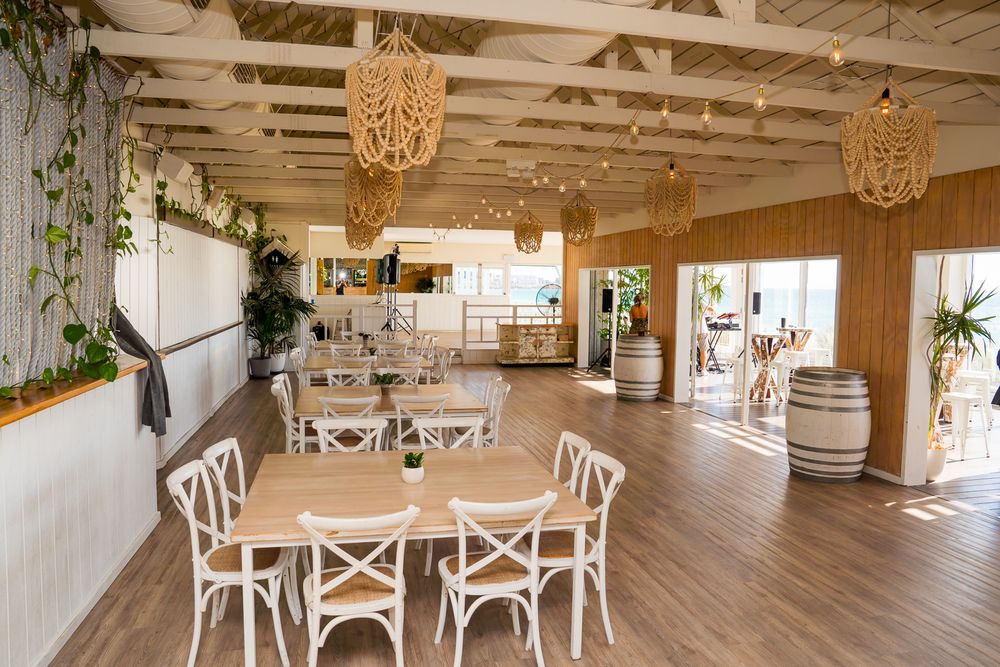 Modern rustic event space with wooden floors, white cross-back chairs, woven pendant lights and wine barrel decor.
