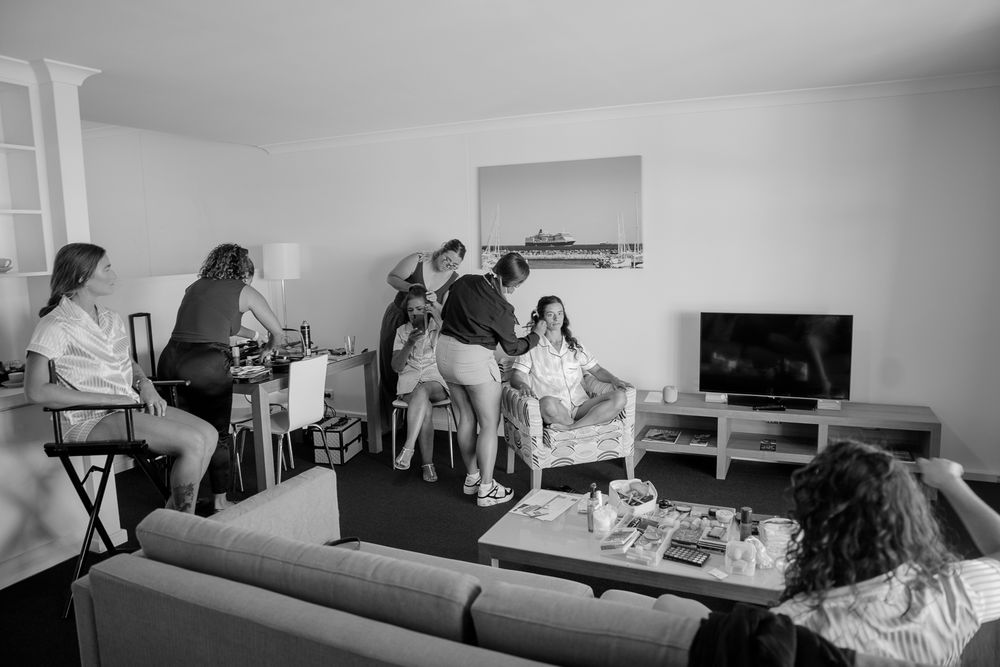 A candid black and white photograph shows people gathered in a modern living room with a TV and couch.