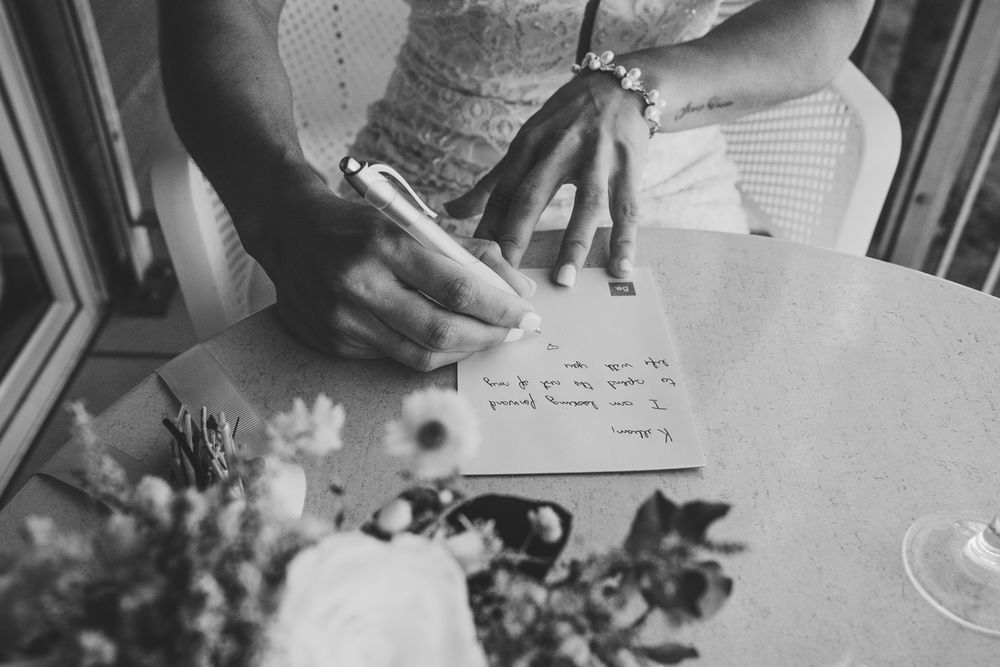 A black and white close-up of hands writing on paper with flower decorations on the table.