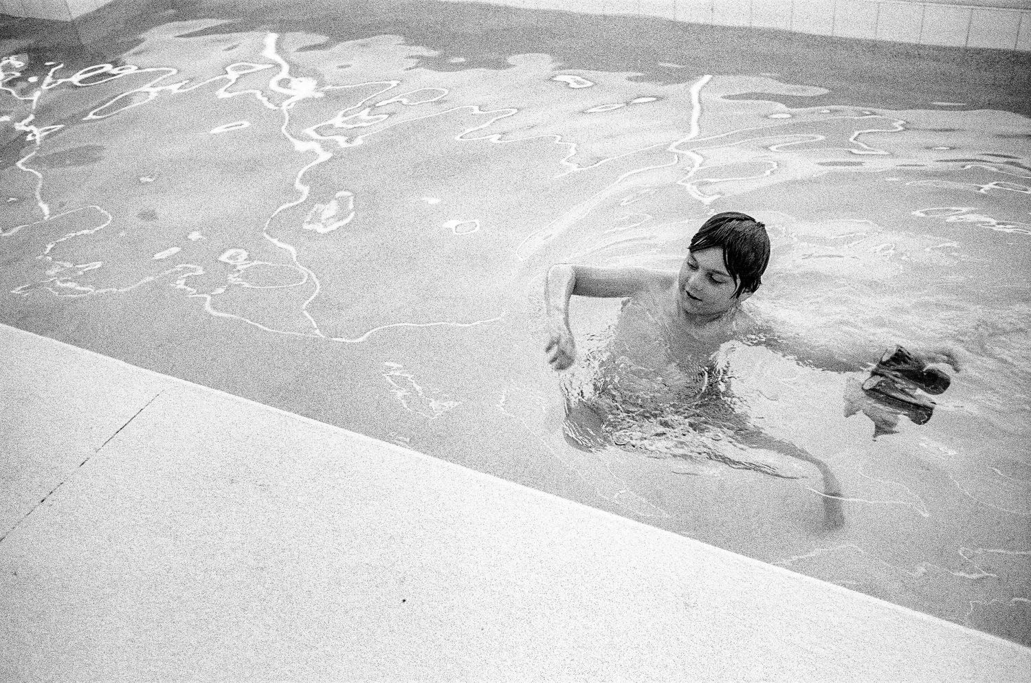 A swimmer enjoys the water in a swimming pool on a bright day, captured in black and white photography.