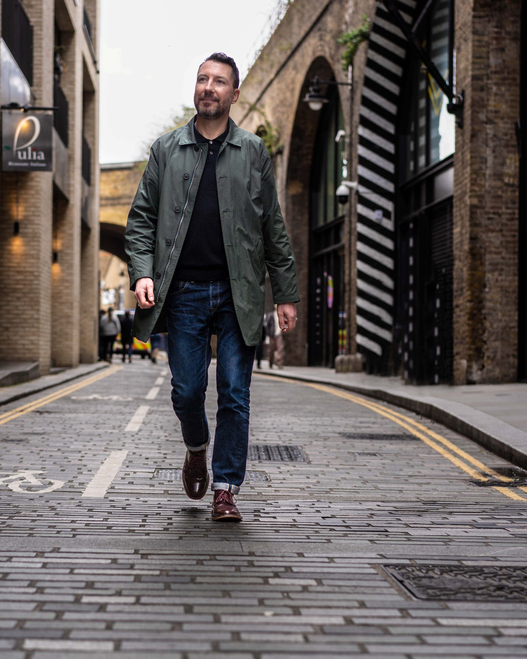 Modern entrepreneur walking down cobblestone street wearing green jacket and jeans on a London personal branding photoshoot