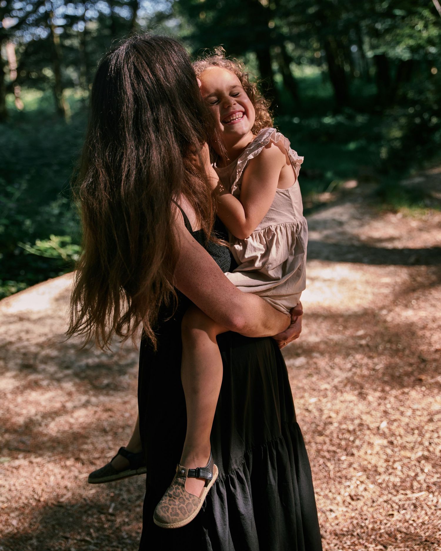 A tender embrace between parent and child on a sunlit forest path.