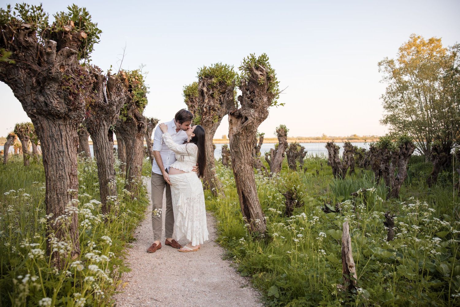 Pregnant couple kissing on a path among trees in an outdoor setting.