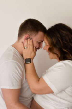 Intimate moment between couple in white shirts sharing a tender touch against neutral wall.