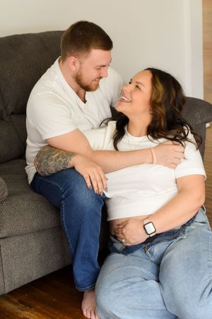 Couple sharing an intimate moment while sitting together on a gray couch in their casual white shirts and jeans.