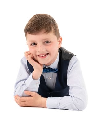 A child in formal attire lies on white background in three different poses, smiling and looking at camera.