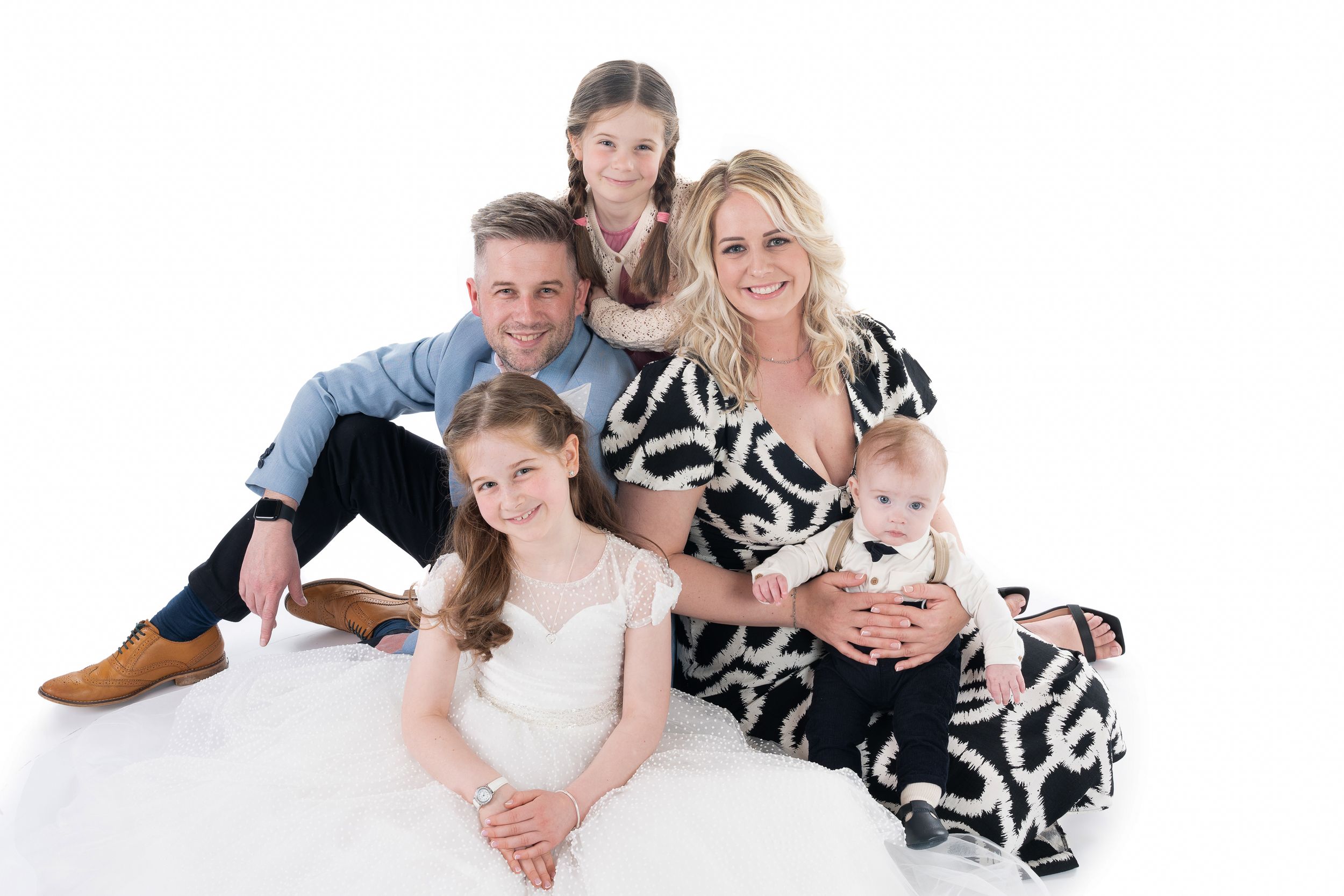 Family members in matching white outfits pose together on a white background for a professional studio portrait.
