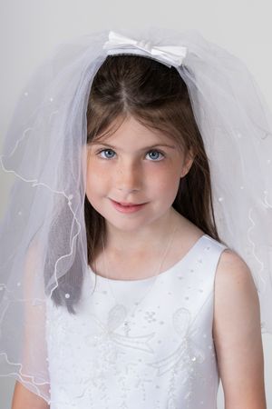 A child wearing a white first communion dress and veil poses for a series of portrait photos.