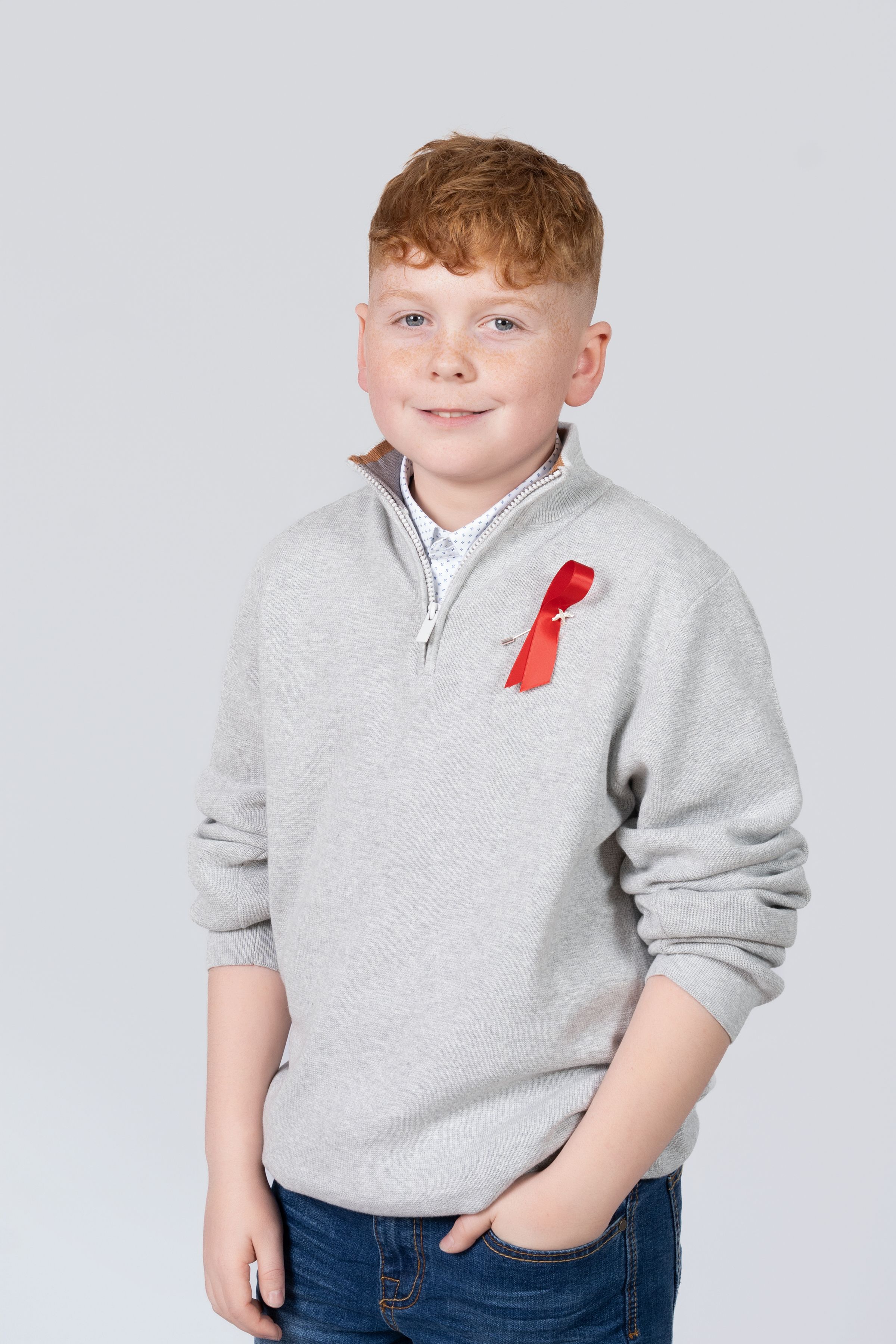 A child wearing a gray sweater with red accent poses casually against a light studio background.