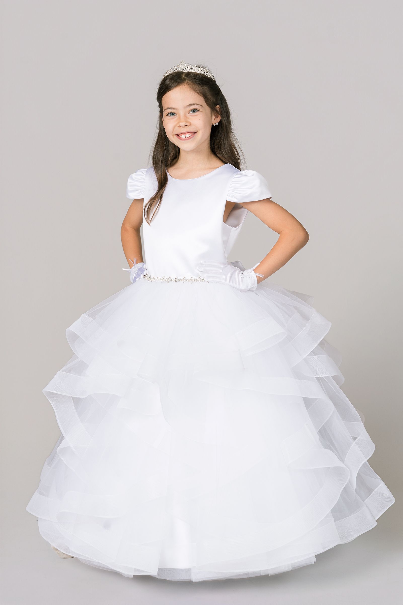 Young girl wearing a beautiful white tiered tulle ball gown with ruffled layers and cap sleeves.