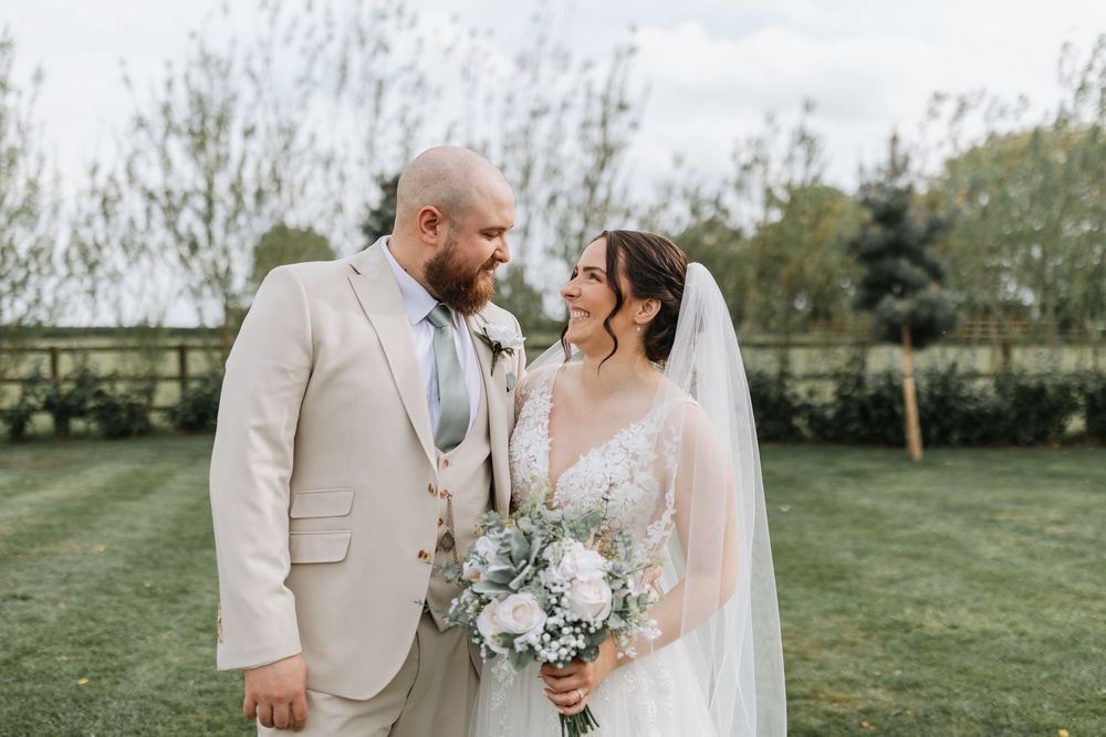 A happy couple shares a tender moment outdoors at their spring garden wedding wearing beige and white attire.