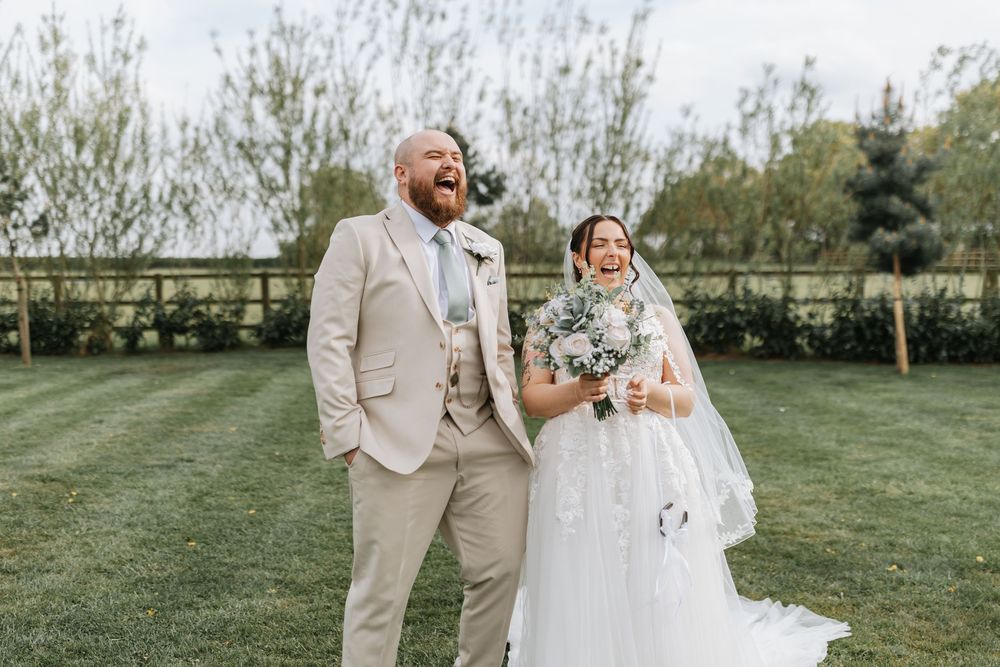 A joyful couple shares a candid moment together on their wedding day while standing on a manicured lawn.