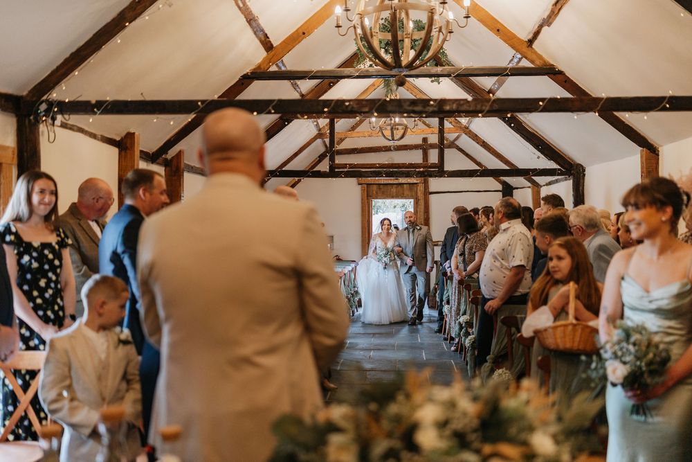 Wedding ceremony takes place in rustic farmhouse venue with exposed wooden beams and chandelier decoration.