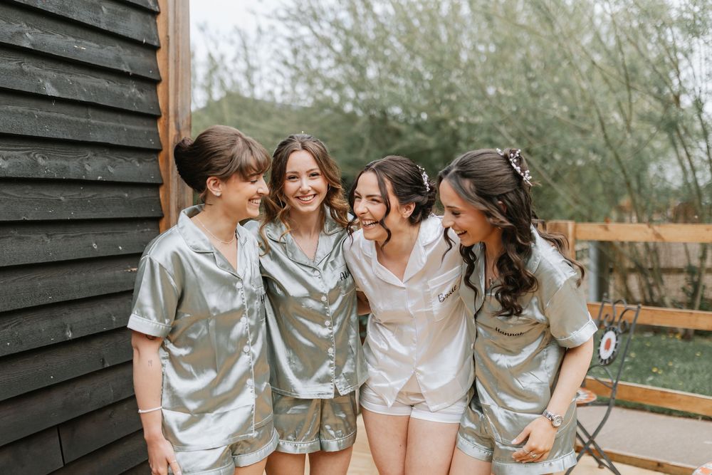 Four friends share a joyful moment together while wearing matching silk loungewear outside a black wooden building.