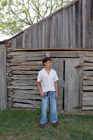 Person stands in casual outfit against weathered wooden barn wall with rustic architectural details.