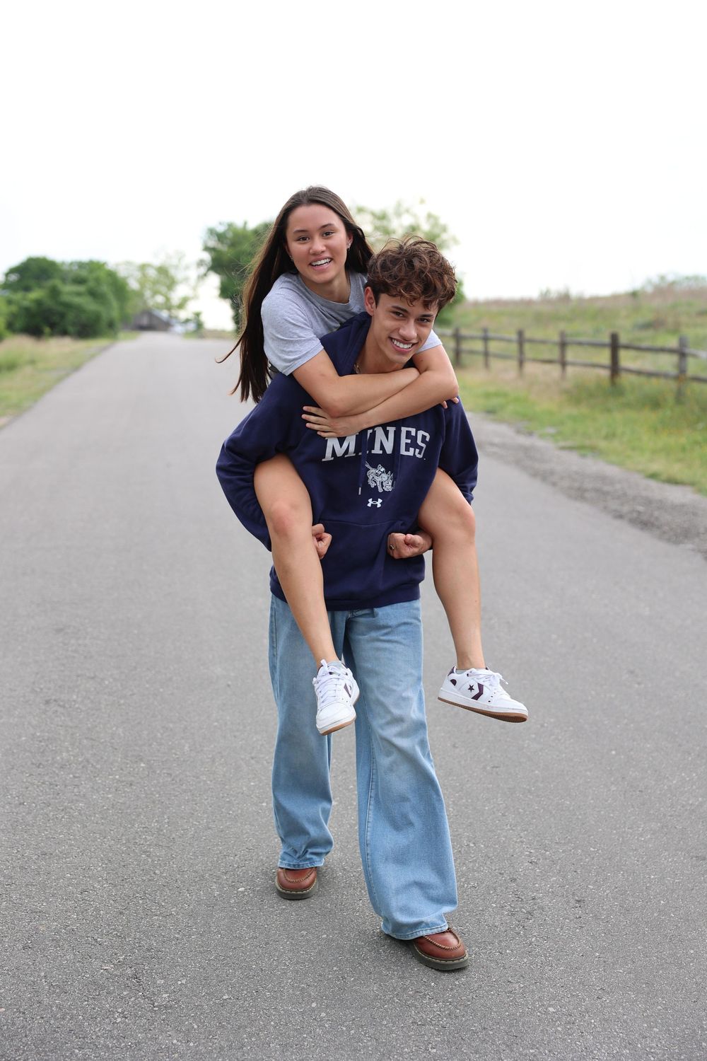 Two friends having fun on a rural road with one giving the other a piggyback ride.