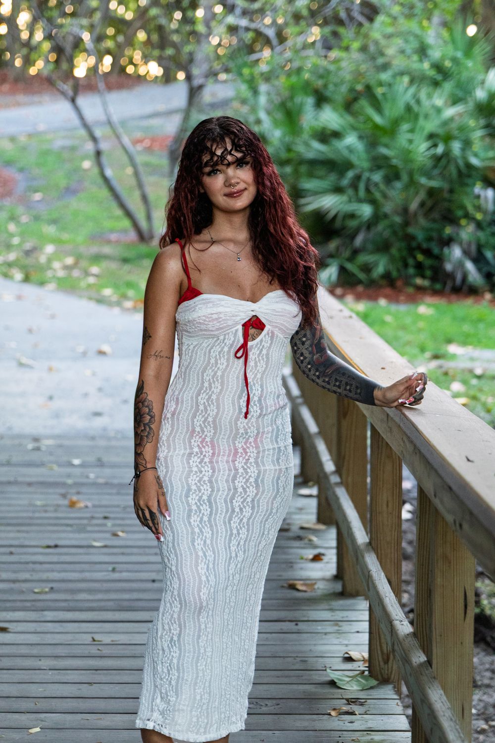 Person in white lace dress poses on wooden boardwalk surrounded by lush greenery.