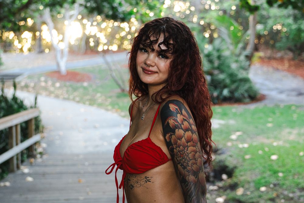 Figure in red attire sits on rustic wooden railing in garden setting.