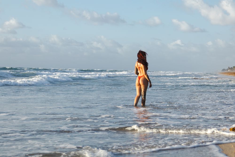 Person strolling on sandy beach with ocean waves in background.