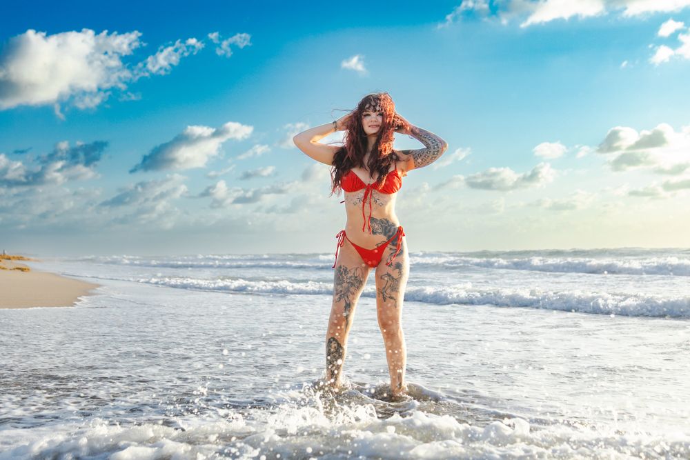 Figure playing in ocean waves on sunny beach with blue sky overhead.