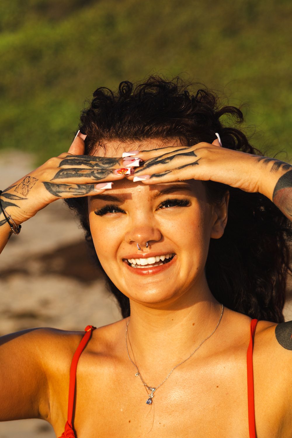 Person shielding eyes from sun on beach during golden hour.