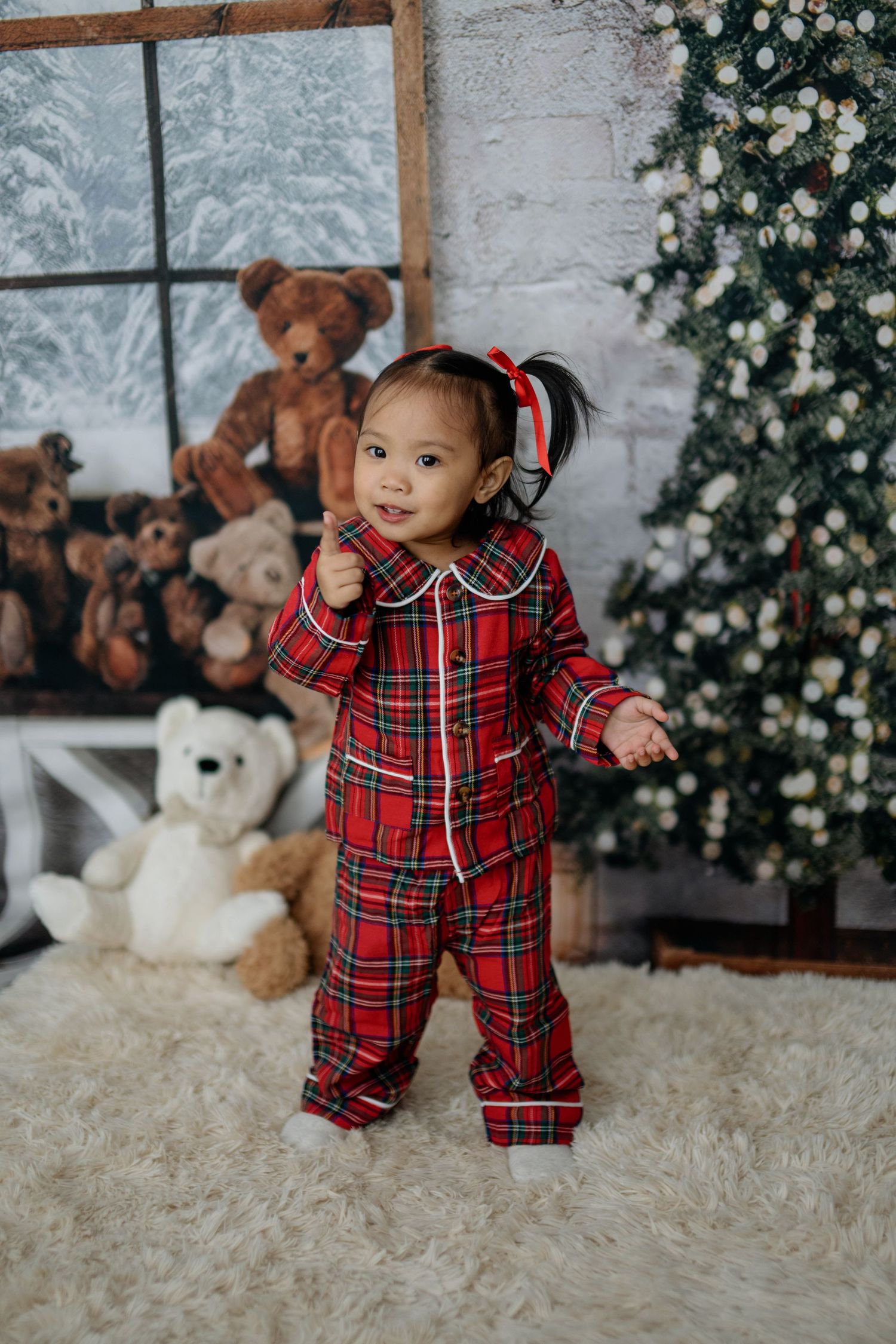 A small child in red plaid pajamas poses for Christmas photos with teddy bears and winter decorations.