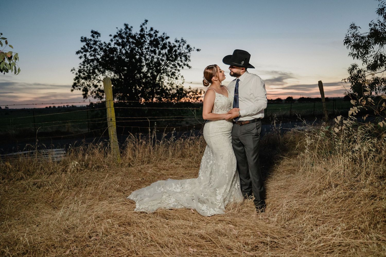 A couple shares an intimate moment at sunset in a golden field with mountains in the background.
