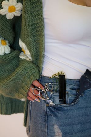 Close-up of blue denim jeans with white daisy flowers and green knit cardigan details.