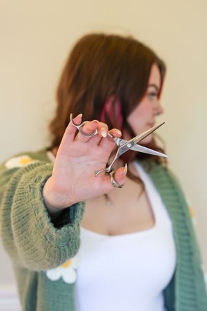 Person wearing green sweater and white top demonstrates different poses while holding scissors near their face.