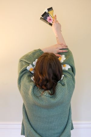 Person wearing a mint green knit sweater shown from behind while holding up their hair in a sequence of poses.