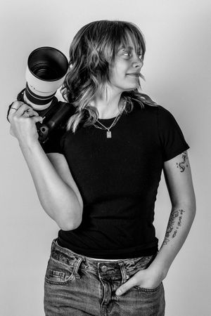 Black and white portrait of photographer holding professional camera lens while wearing casual t-shirt and jeans.