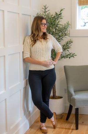 Casual outfit featuring a cream cable knit sweater and dark pants styled in a modern living room setting.