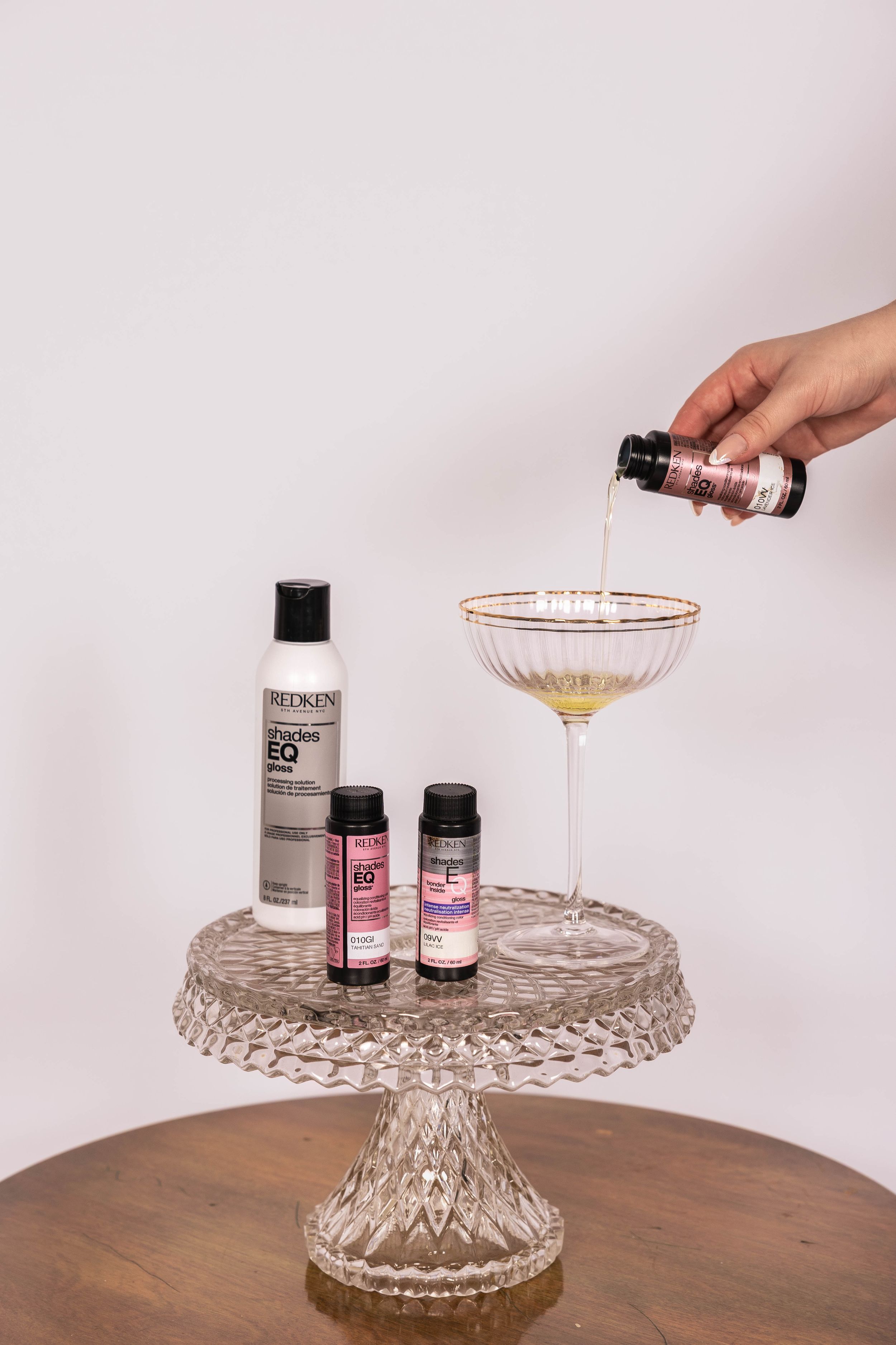 A series of photos showing a cocktail glass being placed on a crystal cake stand with black bottles in the background.