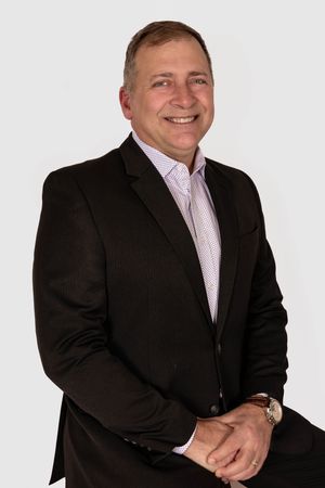 Professional headshot of someone in a black suit and pink dress shirt against white background.