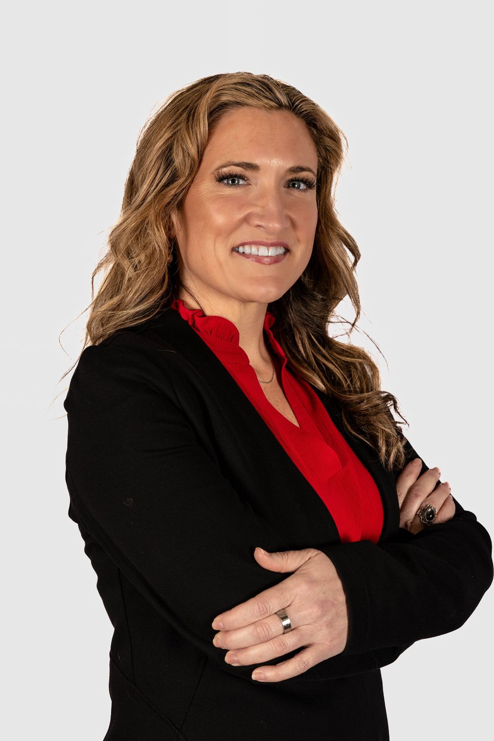 Professional woman in black blazer and red top smiling with arms crossed against white background.
