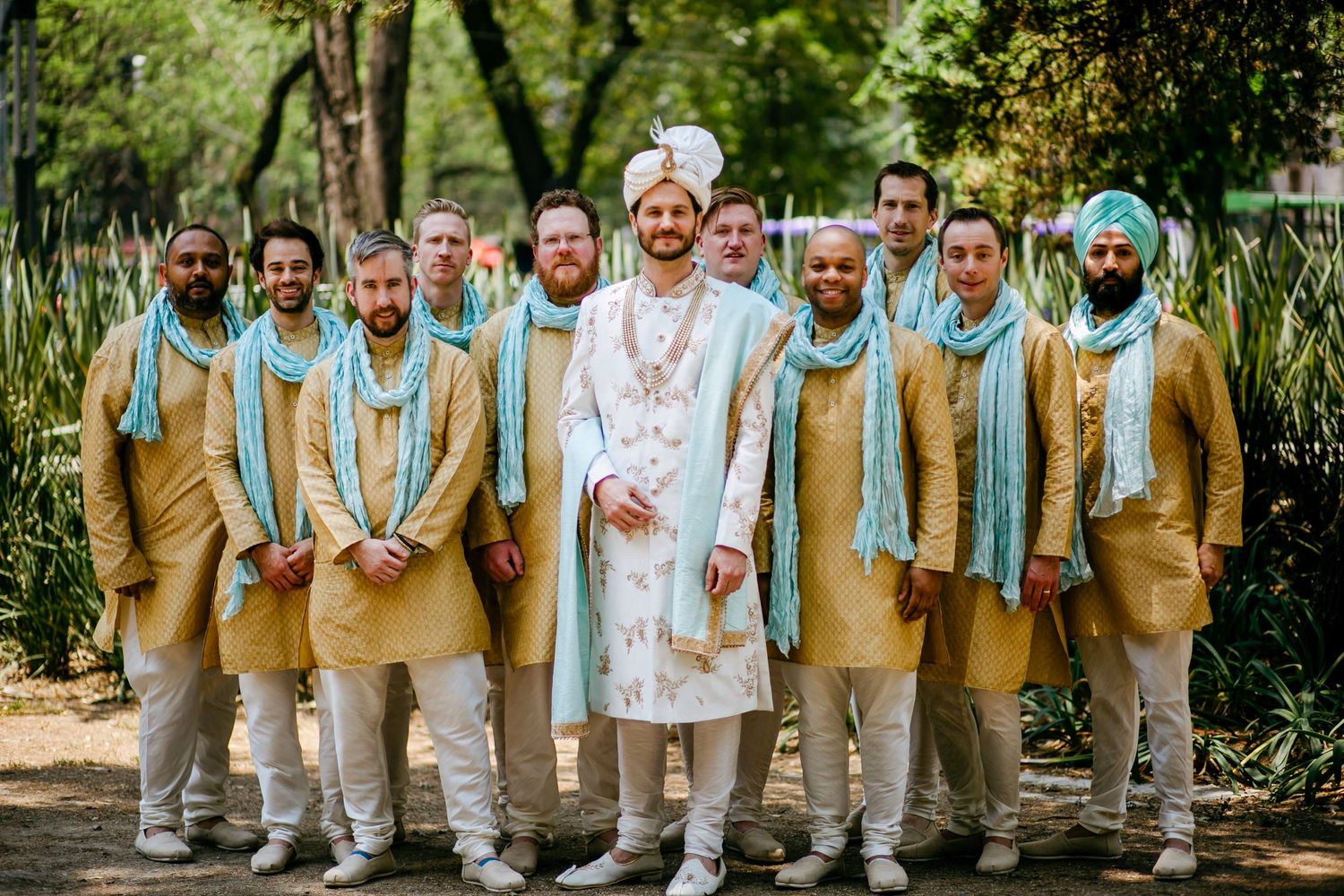 Wedding party in coordinated mint green and beige attire posing in a garden setting.
