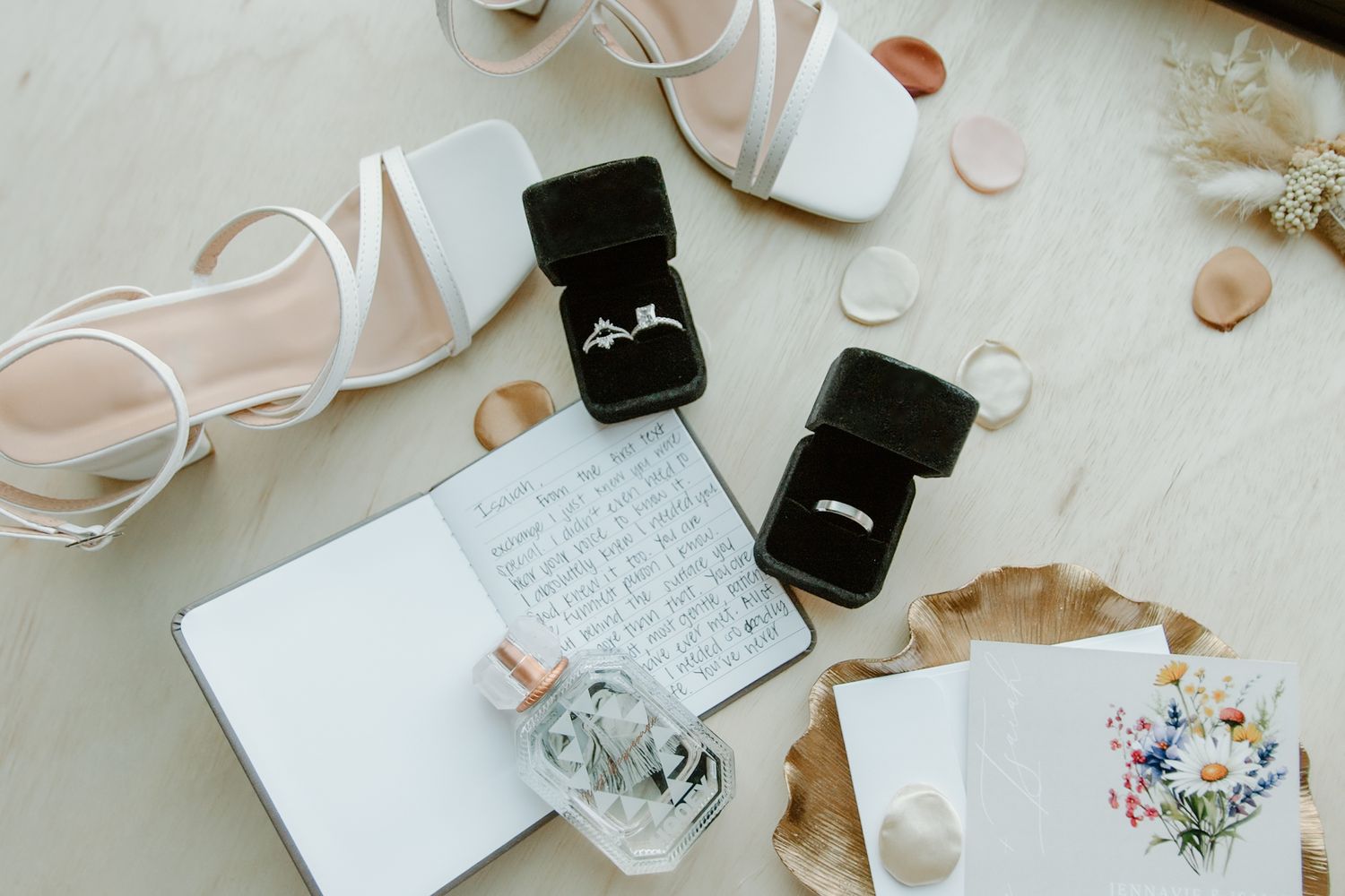 Flatlay of engagement ring boxes, wedding invitations, and delicate floral decor on white background.