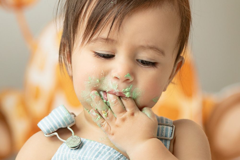A young child in a blue and white striped shirt holds a green leaf up to their nose.