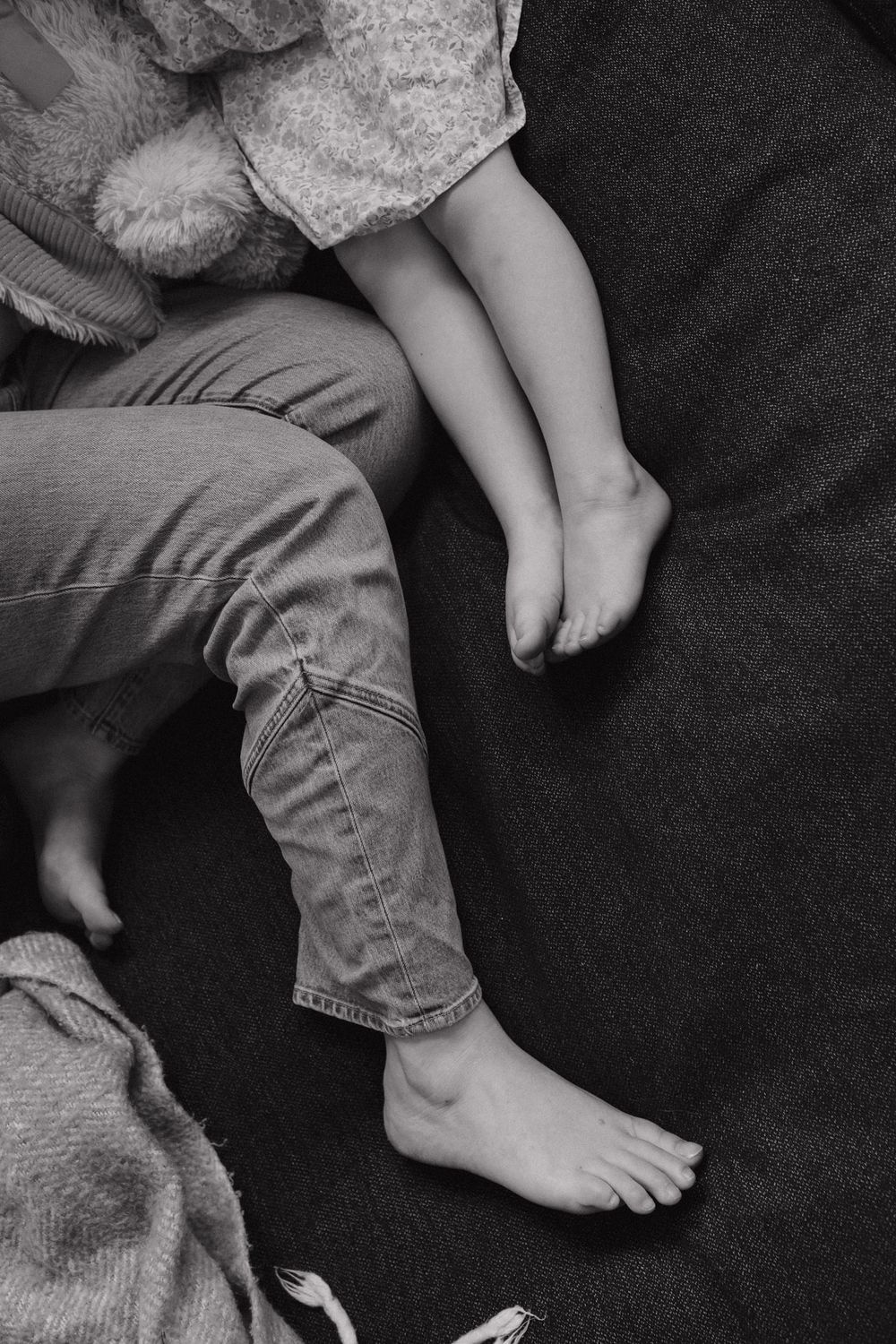 A series of black and white photographs showing small bare feet next to denim jeans on dark fabric.