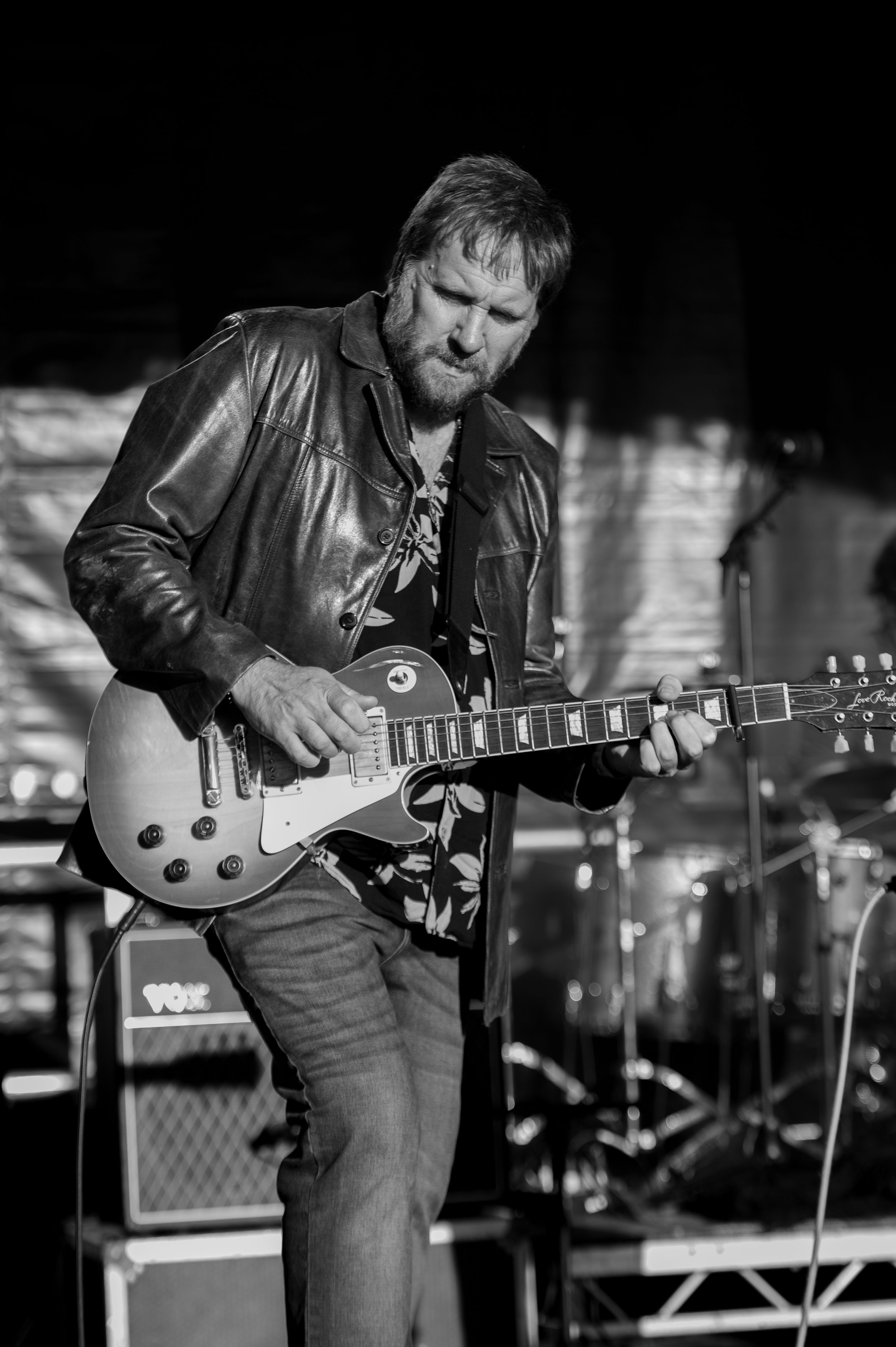 Guitarist in black leather jacket performs on stage with electric guitar during live concert performance.