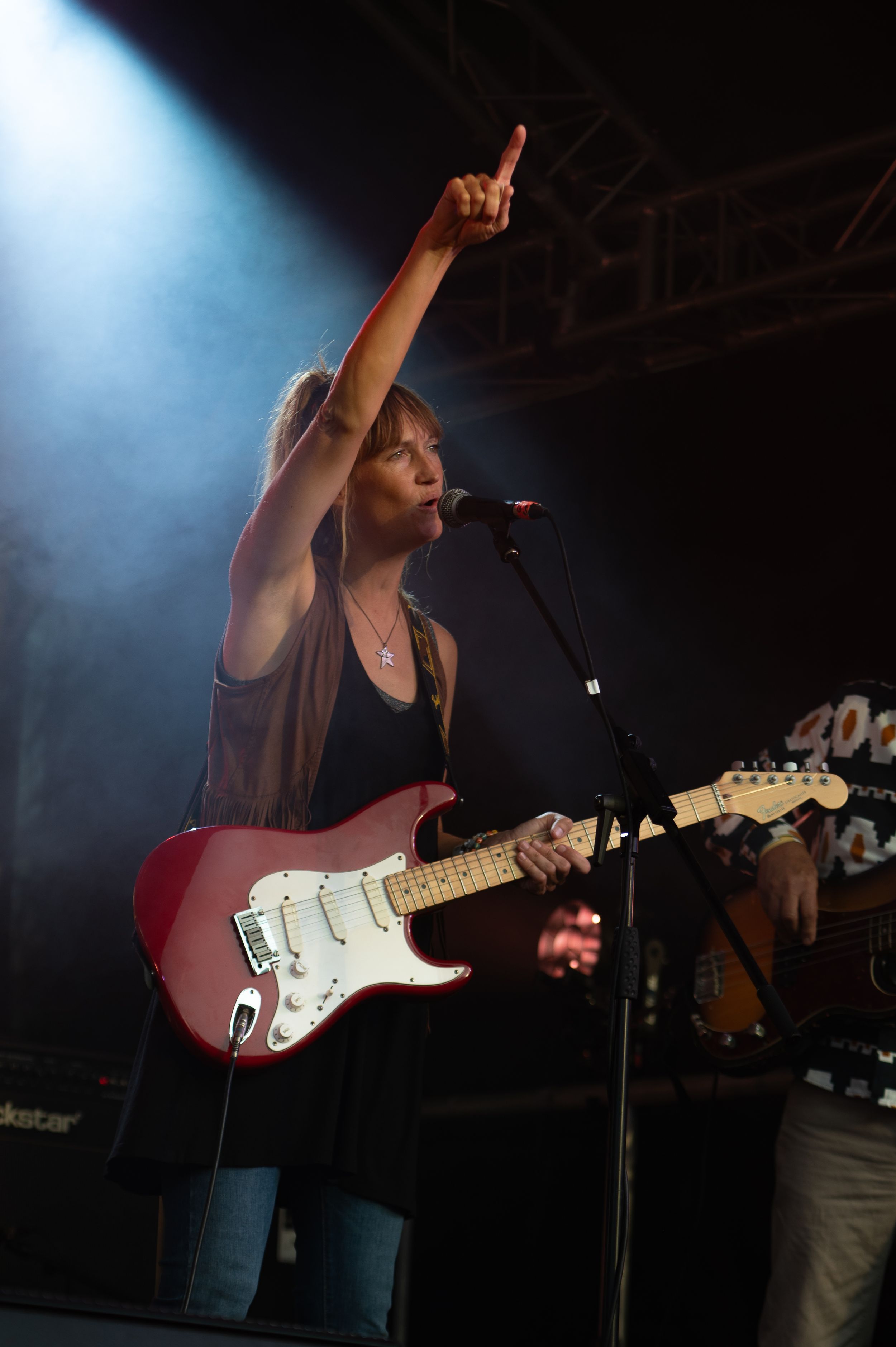 A musician performs on stage with a Fender Stratocaster guitar under dramatic blue lighting during a live concert.