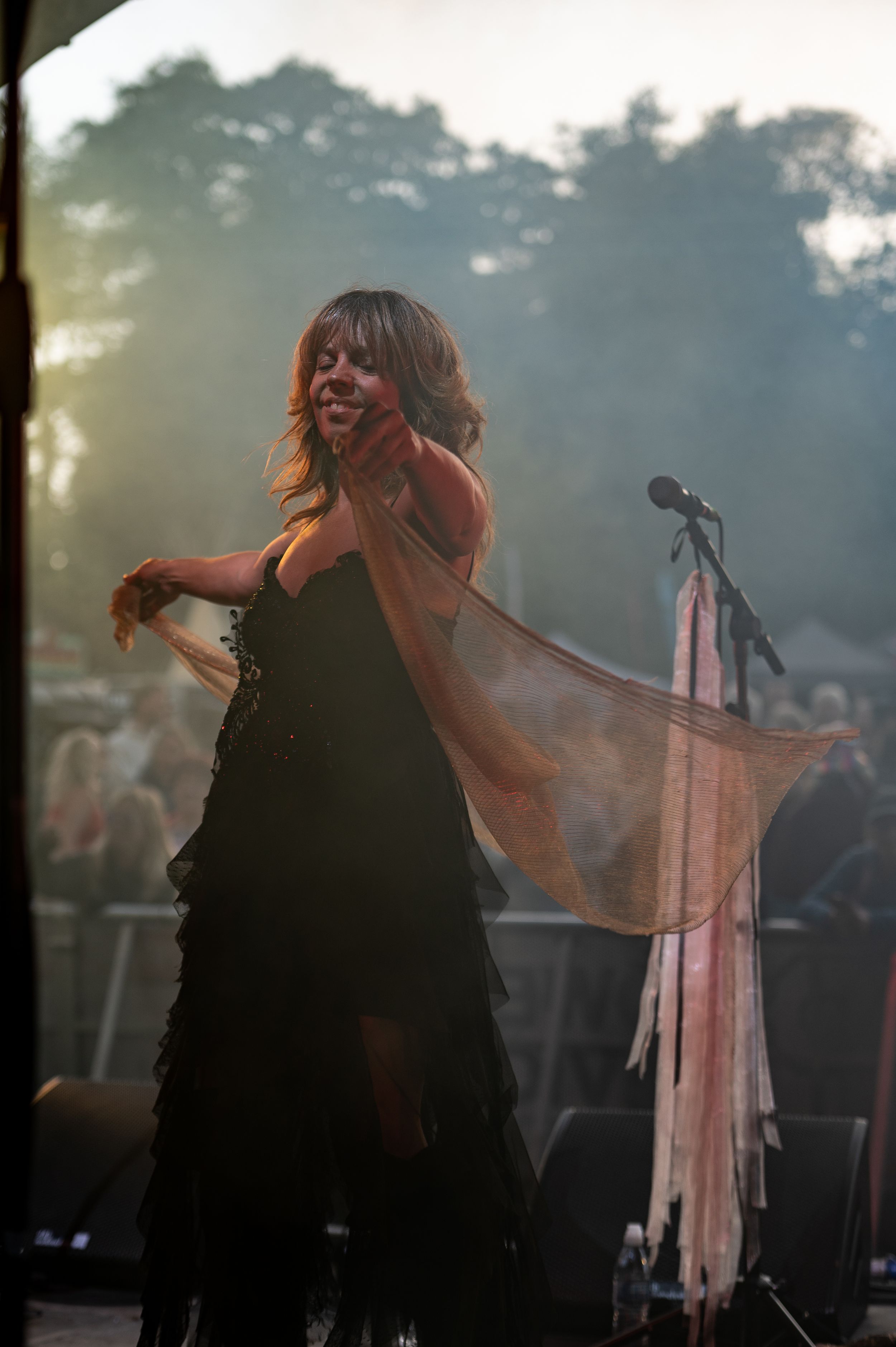 A silhouetted performer dances energetically on stage with flowing fabric during a dramatic sunset performance.