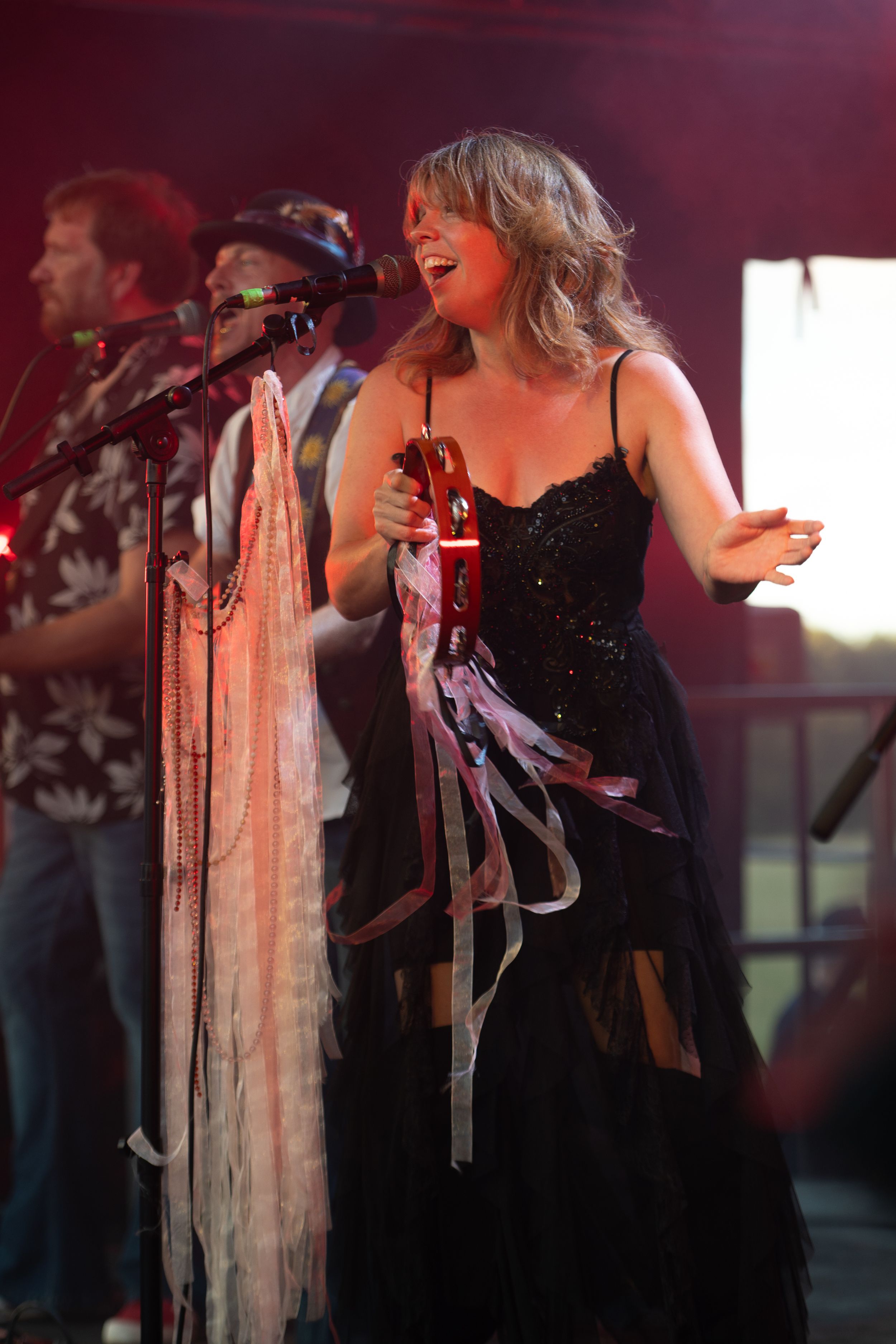 Singer performs on stage in black dress with flowing white ribbons under dramatic red stage lighting.