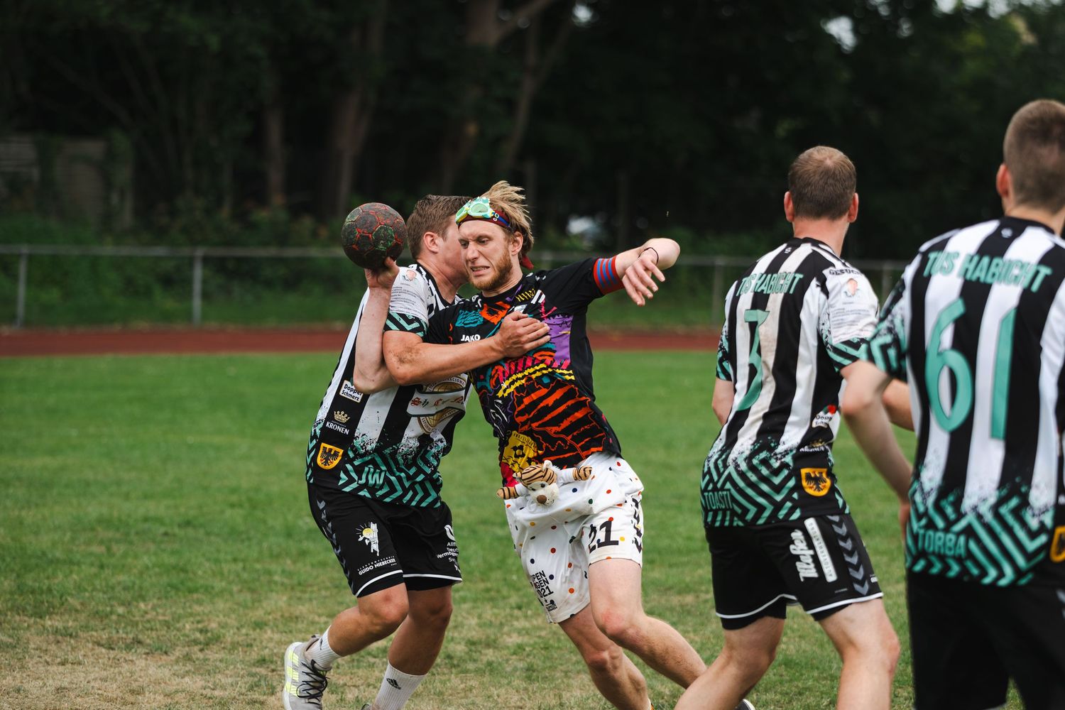 Athletes participate in an outdoor sports event on a sunny green field with spectators watching in the background.