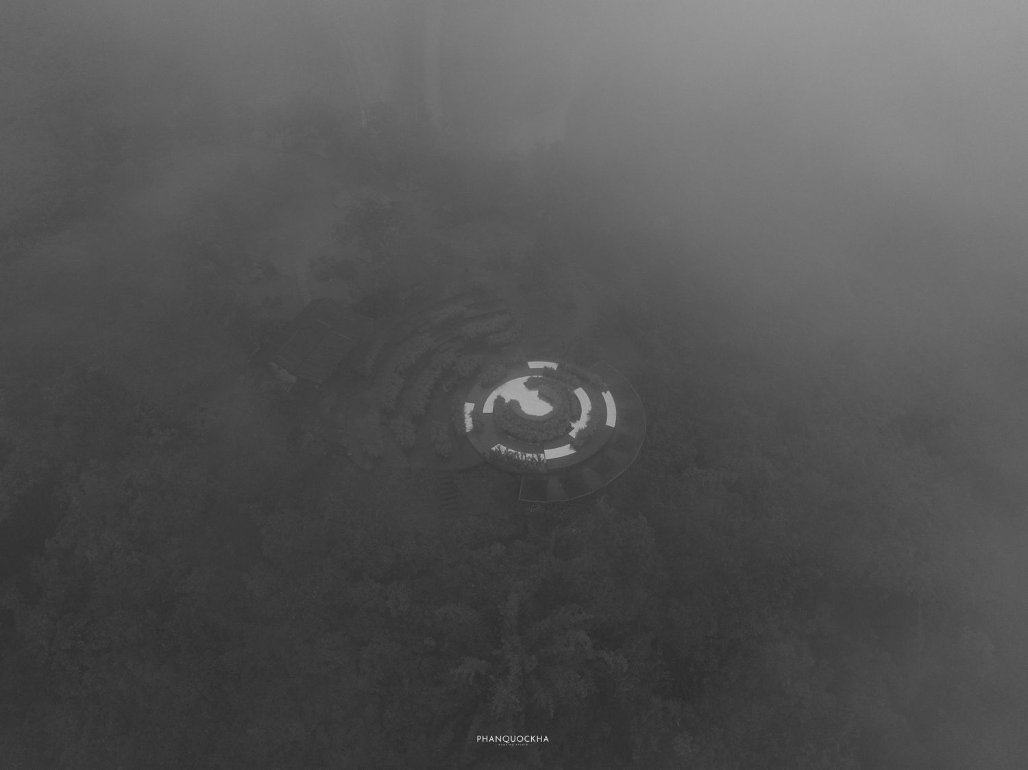 Aerial black and white view of circular garden structure surrounded by misty fog.