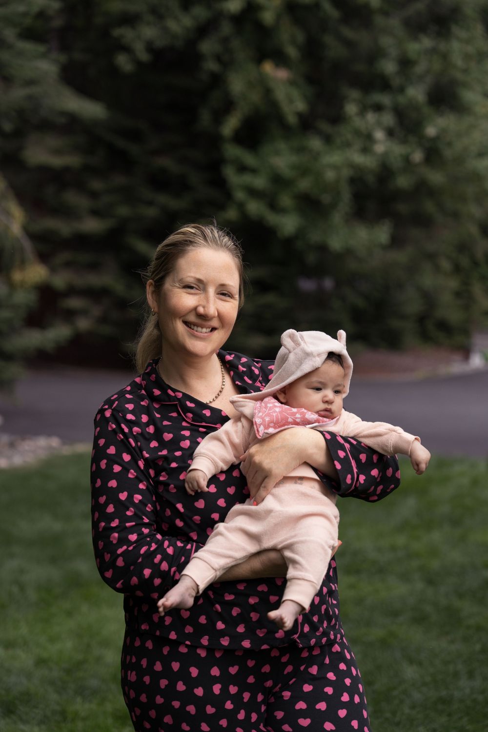 A playful moment captured outdoors as a parent wearing a heart-print dress holds and interacts with a baby in pink clothing.