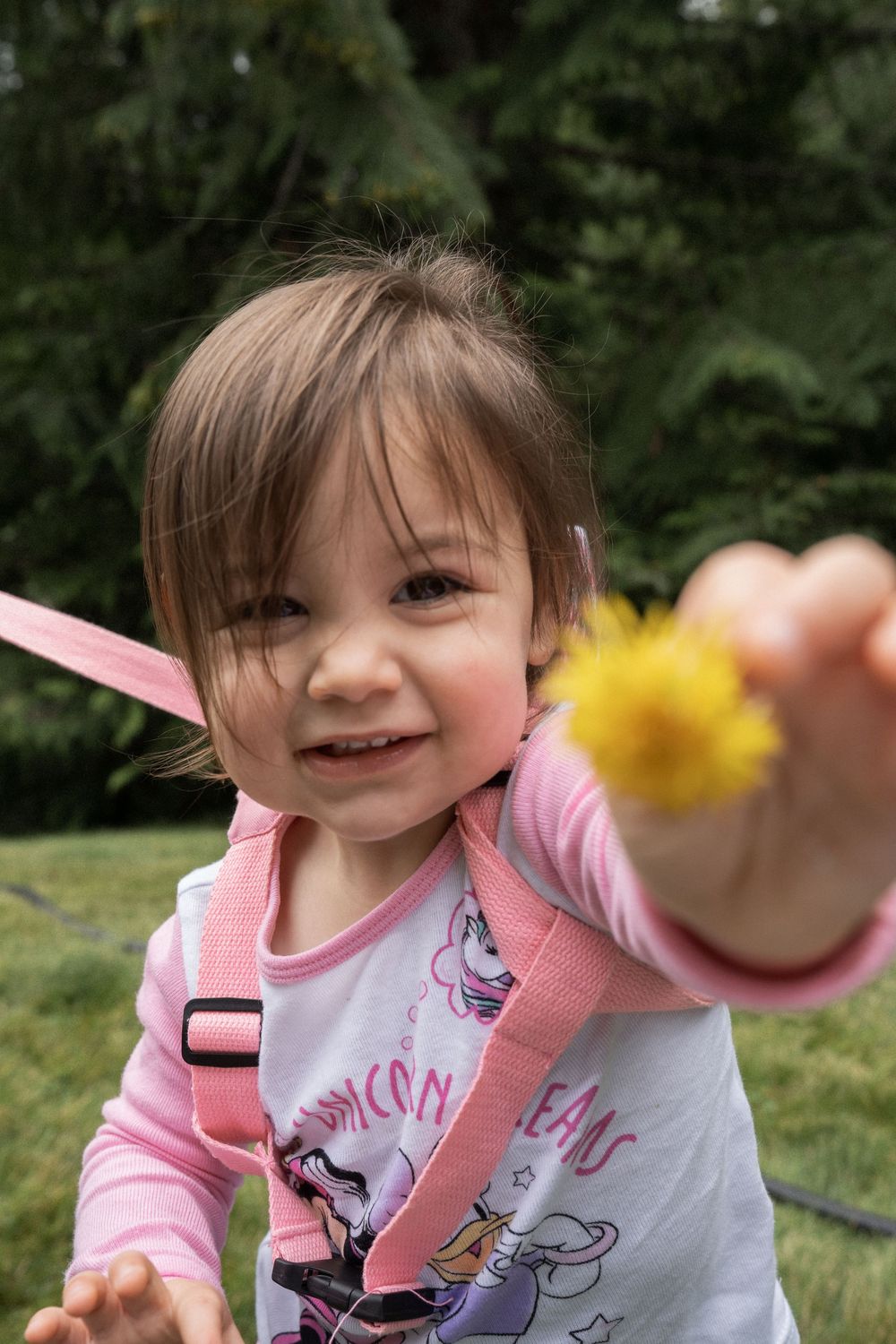A child wearing a pink unicorn outfit plays with a yellow toy in a grassy outdoor setting.